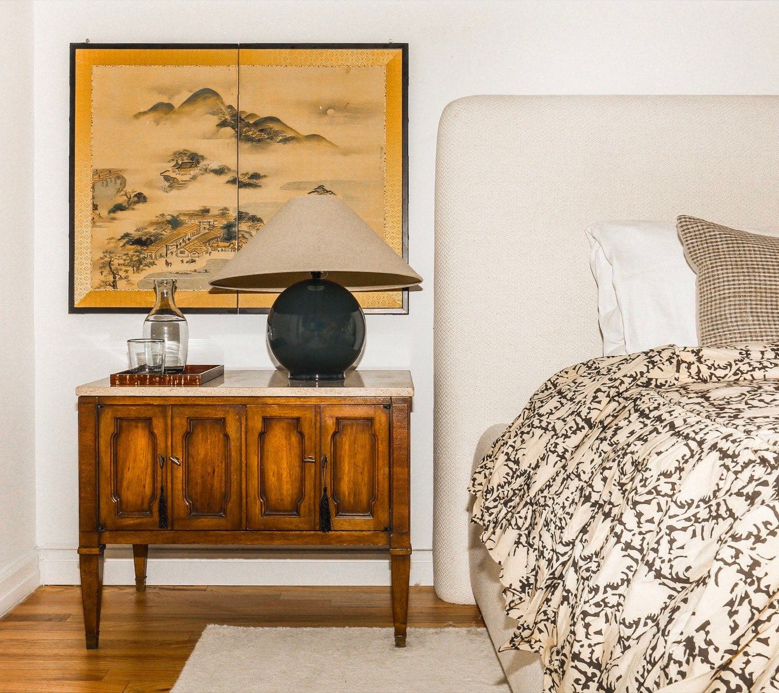 Bedside vignette with a vintage wood nightstand, globe lamp, and Japanese landscape screen