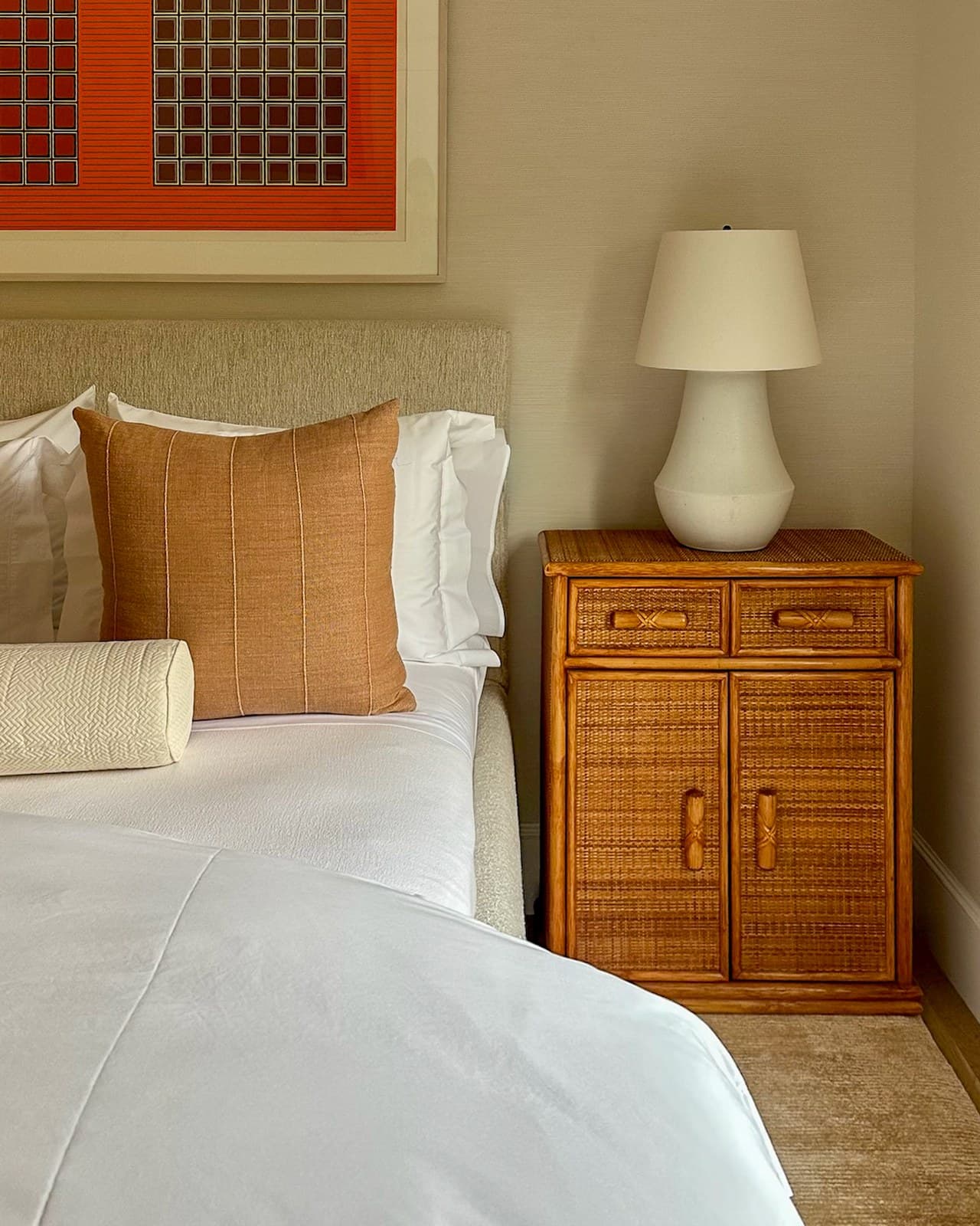 Warm bedroom with white bedding, terracotta pillows, and a rattan nightstand